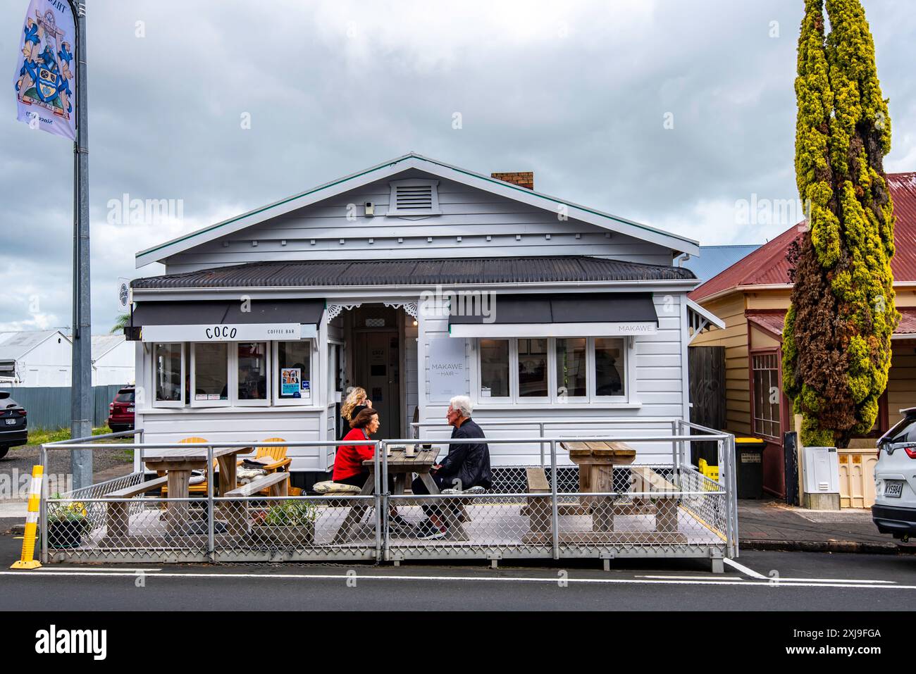 Menschen sitzen im Wind vor einem umgebauten Holzbungalow, heute ein Café in der Stadt Themse auf der Nordinsel Neuseelands Stockfoto