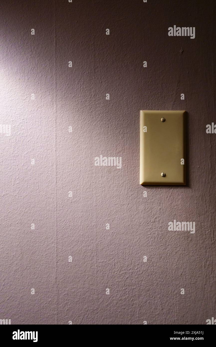 Ein Schild an der Wand, das eine elektrische Steckerplatte im Schatten bedeckt. Stockfoto