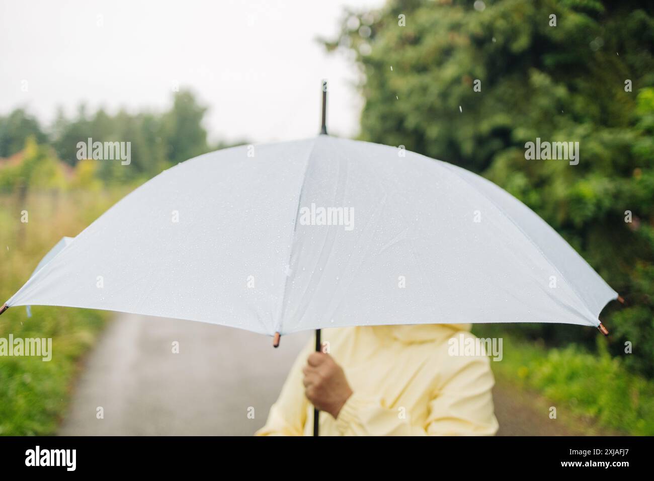 Porträt einer fröhlichen, schönen älteren Frau aus den 50er Jahren, die mit Regenschirm unter Regen steht und nach Herbstregen lächelt Stockfoto