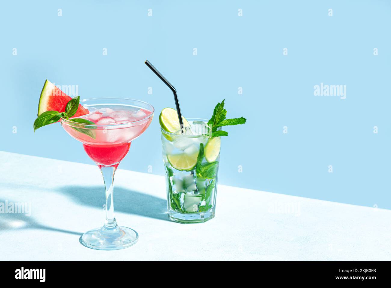 Trendiges Mojito und rosa Margarita Cocktail Drink mit Wassermelone, Minze und Eis auf hellblauem Hintergrund, Sonnenlicht, Kopierraum. Kreativer Sommercocktail Stockfoto