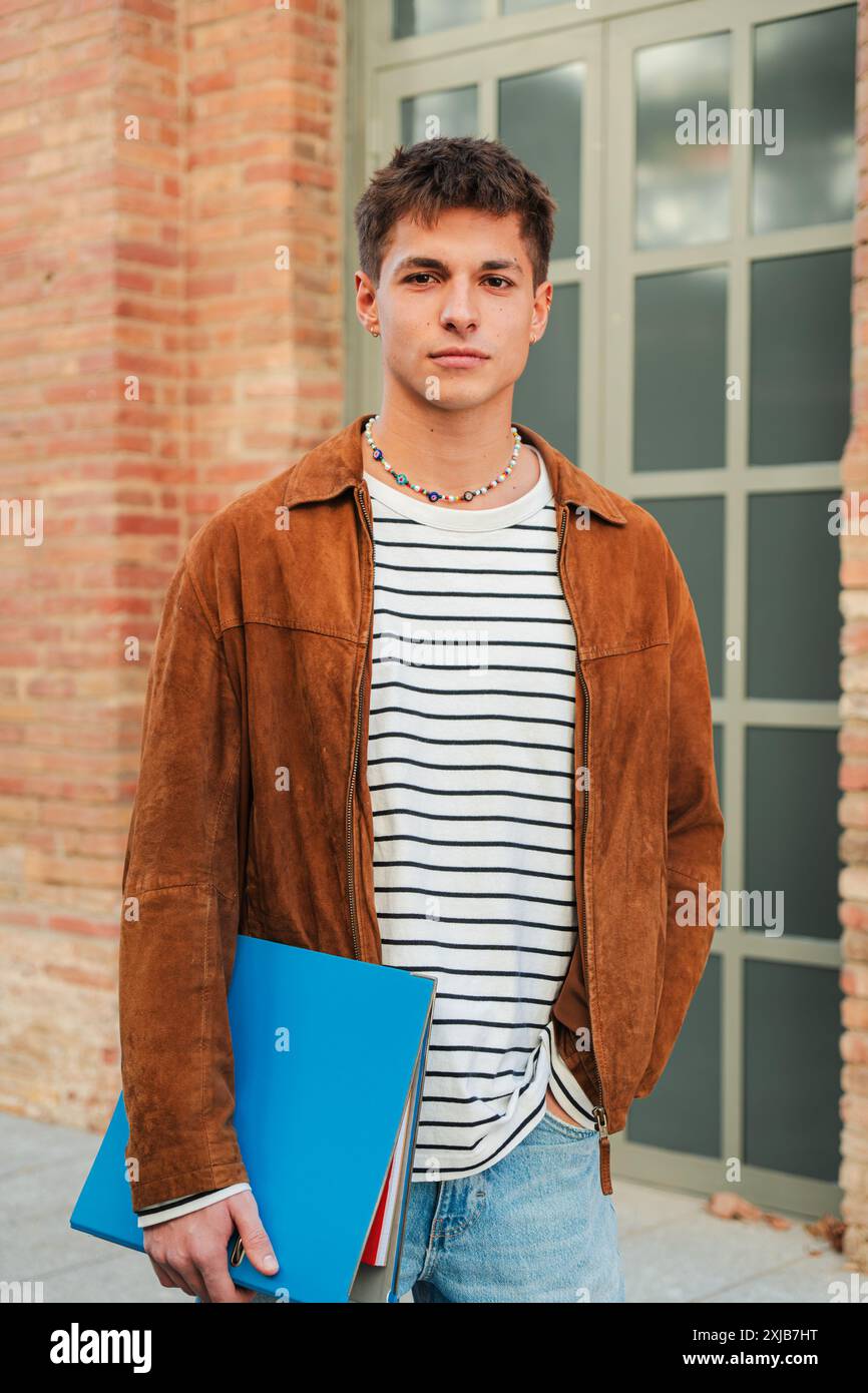 Junger Erwachsener an der Akademie. Individuelles Porträt eines ernsthaften Schuljungen, der in die Kamera blickt, die in der High School steht. Ein nachdenklicher männlicher Student im Teenageralter starrt nach vorne. Nachdenklicher Mann auf dem Universitätscampus. Hochwertige Fotos Stockfoto