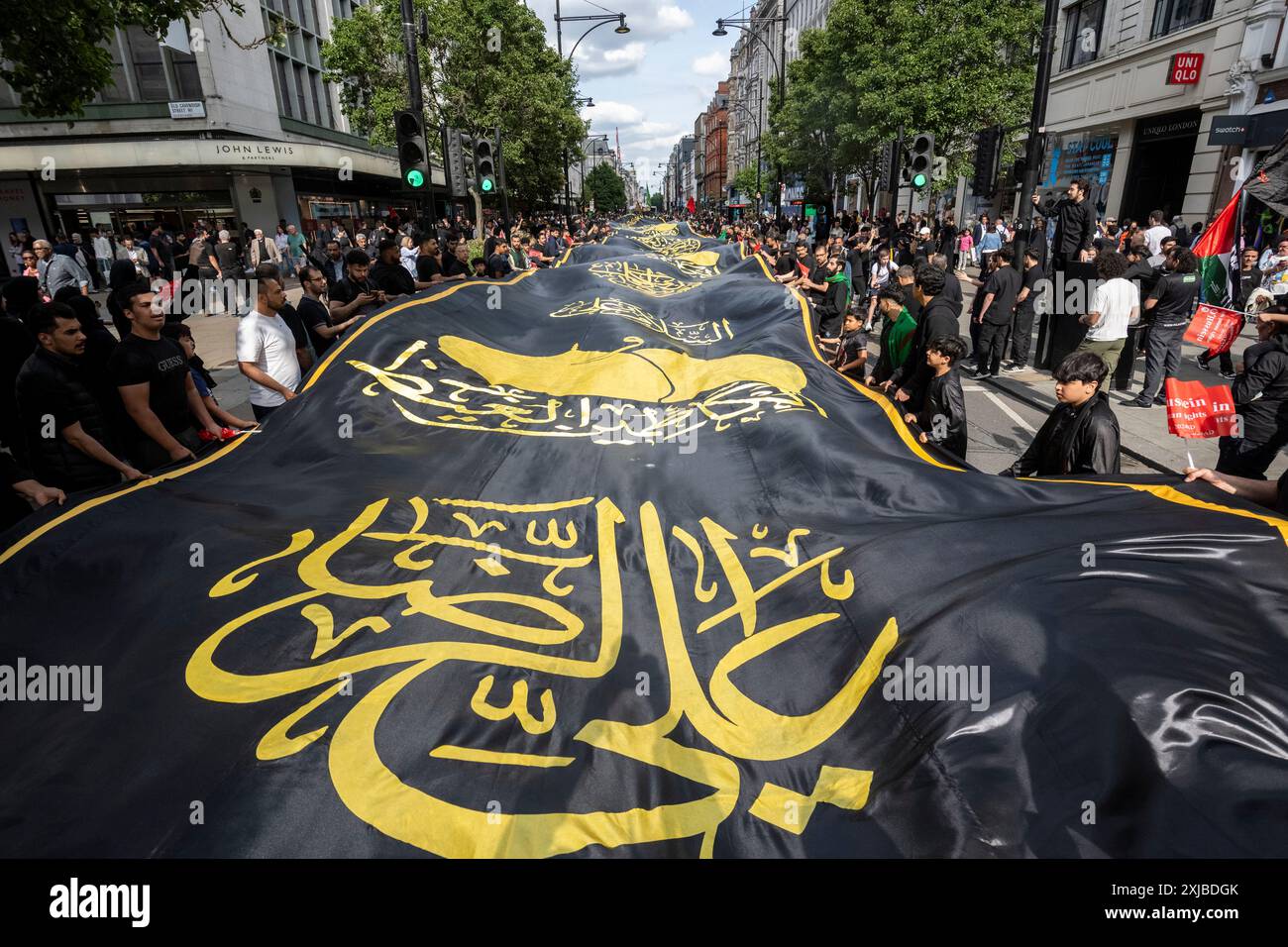 London, Großbritannien. 17. Juli 2024. Eine riesige Flagge wird auf der Oxford Street getragen, während Zehntausende britische Muslime an dem Martyrium von Hussain, dem Enkel des Propheten Mohammed, am zehnten Tag auf Arabisch, erinnern. Dieses friedliche Ereignis wird weltweit jährlich gefeiert, bei dem Menschen in Erinnerung gehen. In der Hauptstadt führte der Weg von Marble Arch nach Whitehall. Quelle: Stephen Chung / Alamy Live News Stockfoto