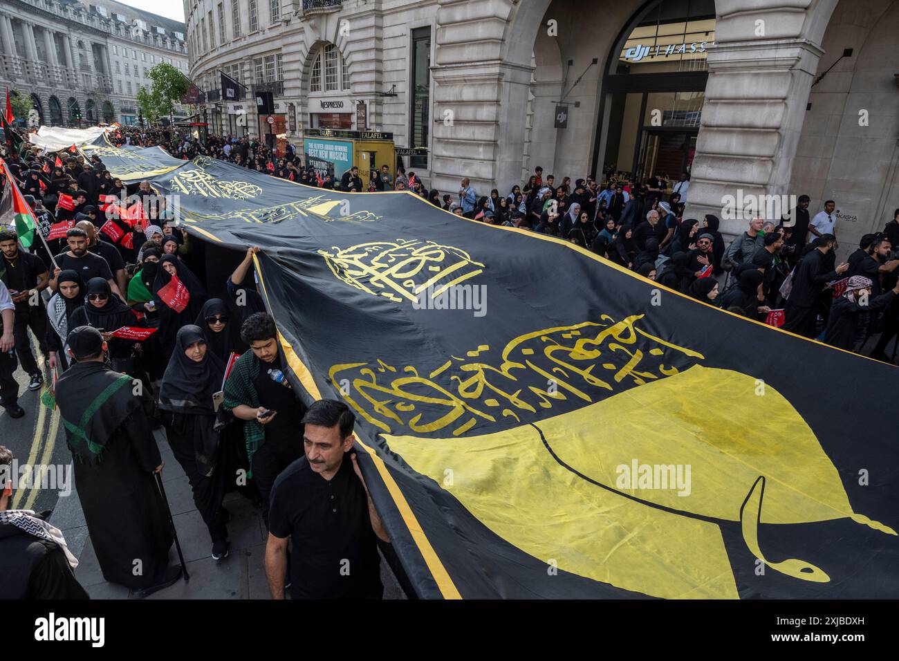 London, Großbritannien. 17. Juli 2024. Eine riesige Flagge wird auf der Regent Street getragen, während Zehntausende britische Muslime an dem Martyrium von Hussain, dem Enkel des Propheten Mohammed, an dem zehnten Tag auf Arabisch, erinnern. Dieses friedliche Ereignis wird weltweit jährlich gefeiert, bei dem Menschen in Erinnerung gehen. In der Hauptstadt führte der Weg von Marble Arch nach Whitehall. Quelle: Stephen Chung / Alamy Live News Stockfoto