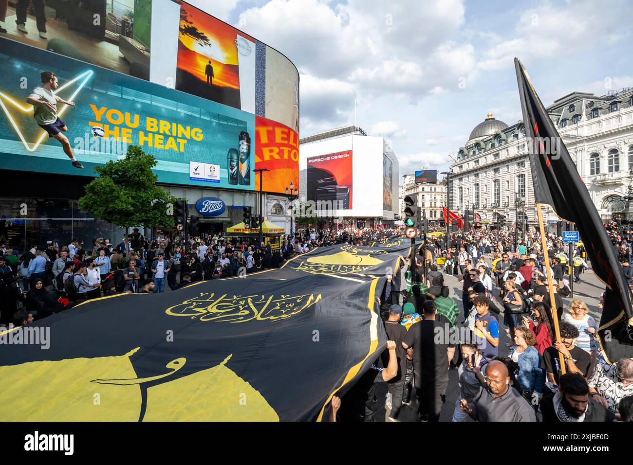 London, Großbritannien. 17. Juli 2024. Eine riesige Flagge wird durch den Piccadilly Circus getragen, während Zehntausende britische Muslime an dem Martyrium von Hussain, dem Enkel des Propheten Mohammed, an dem zehnten Tag auf Arabisch, erinnern. Dieses friedliche Ereignis wird weltweit jährlich gefeiert, bei dem Menschen in Erinnerung gehen. In der Hauptstadt führte der Weg von Marble Arch nach Whitehall. Quelle: Stephen Chung / Alamy Live News Stockfoto