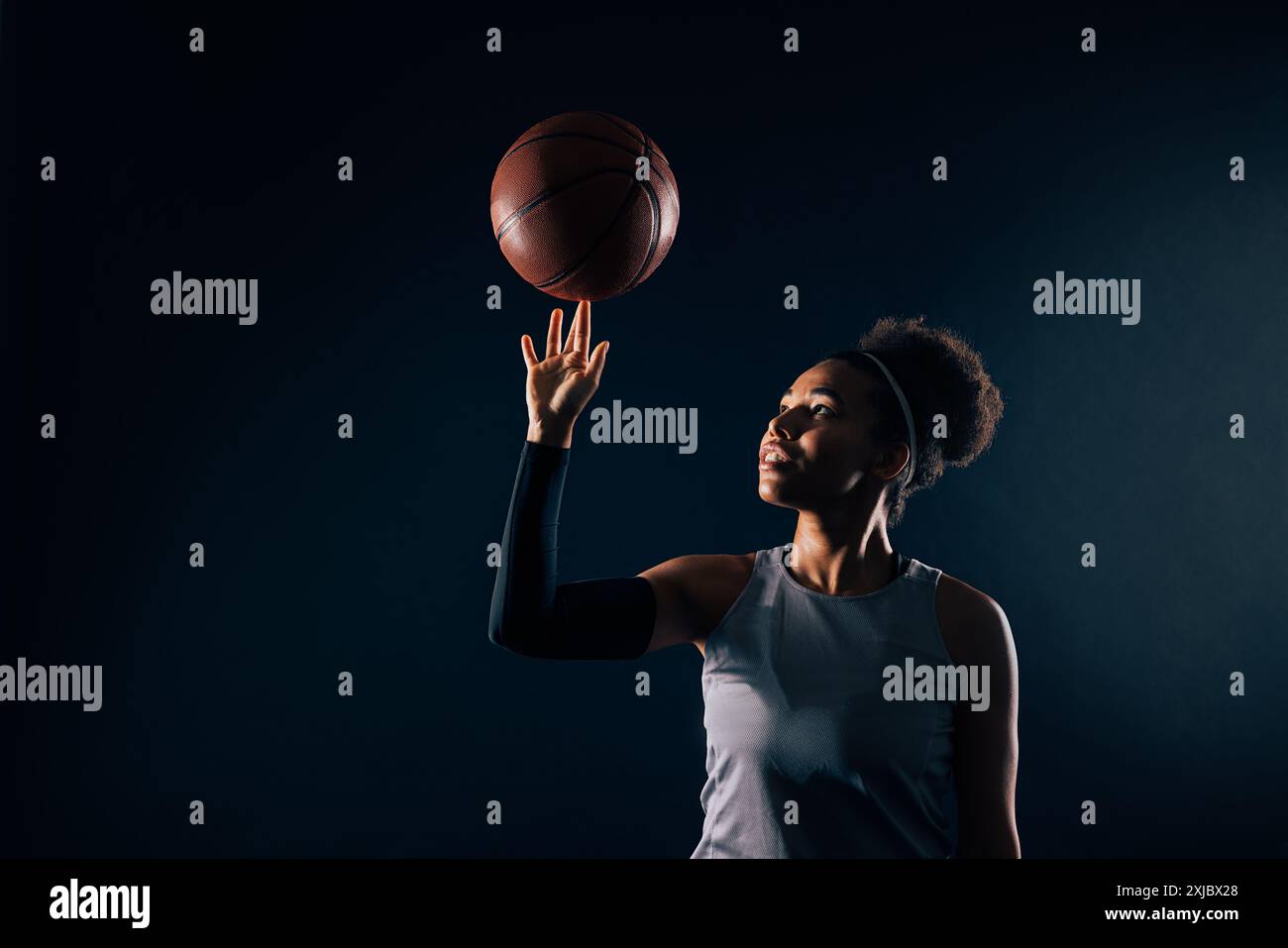 Studio-Aufnahme einer jungen Sportlerin, die Basketball am Finger dreht. Professioneller Basketballspieler auf schwarzem Hintergrund. Stockfoto