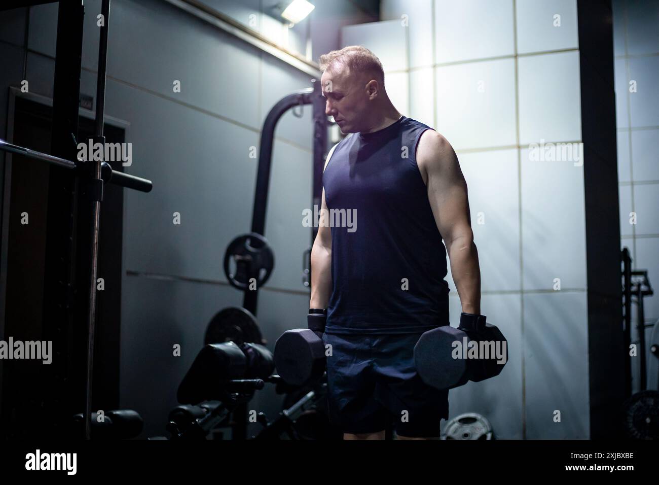 Ein Mann in einem schwarzen Tanktop hebt Gewichte während eines Fitnesstrainings. Stockfoto