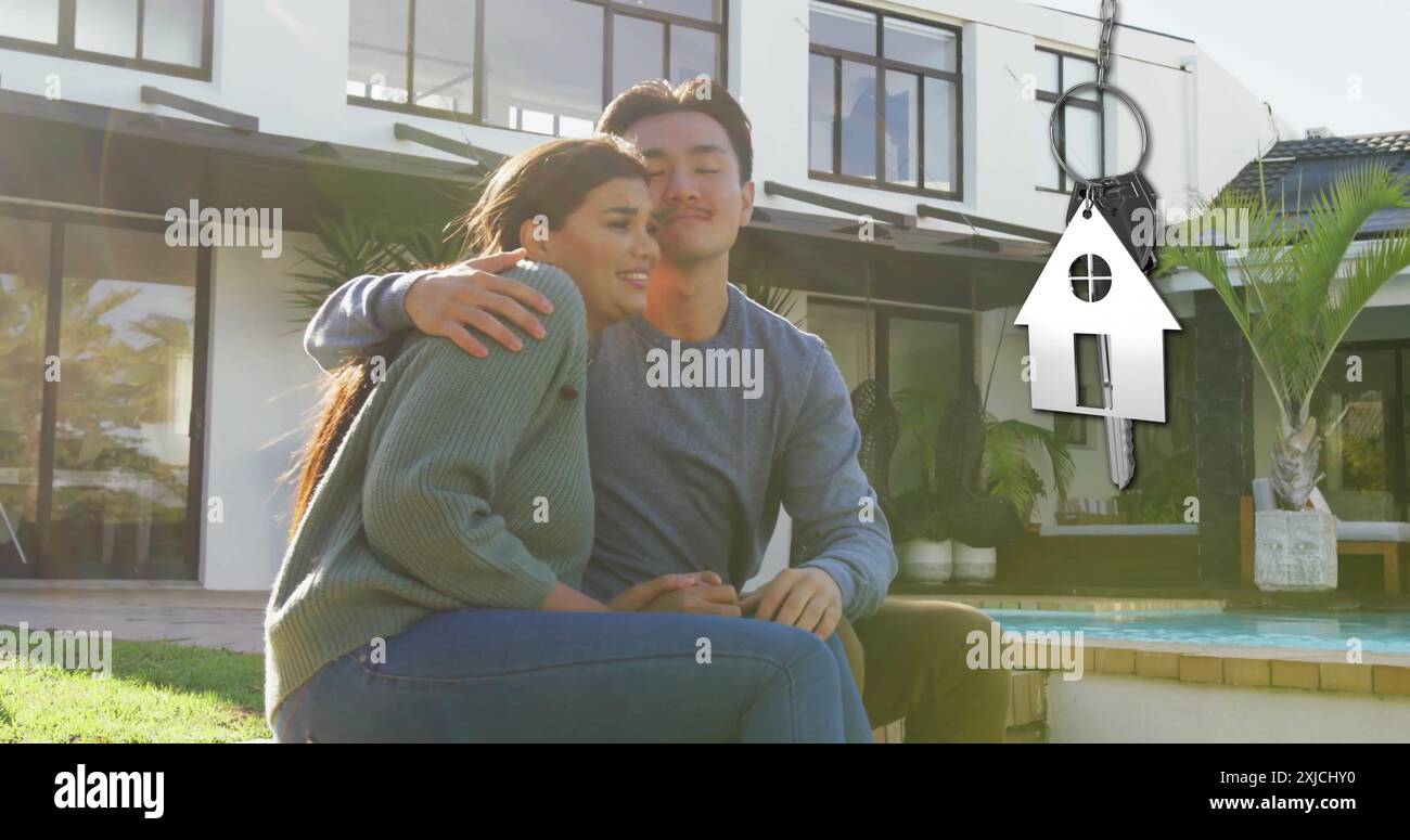 Bild des silbernen Hausschlüssels und Schlüsselanhängers über glücklichen, vielfältigen Paaren im Garten zu Hause Stockfoto