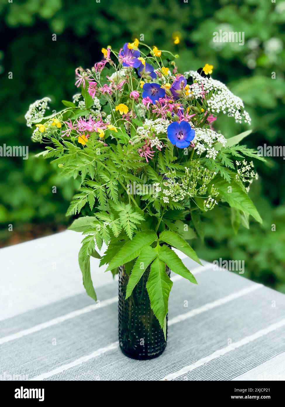 Eine fesselnde Ausstellung von bunten Wildblumen, lila, gelb und weiß, angeordnet in einer eleganten schwarzen Glasvase. Stockfoto