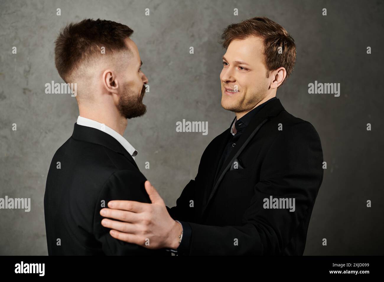 Zwei Männer in edlen Anzügen teilen sich einen zärtlichen Moment, einer legt seine Hand sanft auf die andere Schulter. Stockfoto