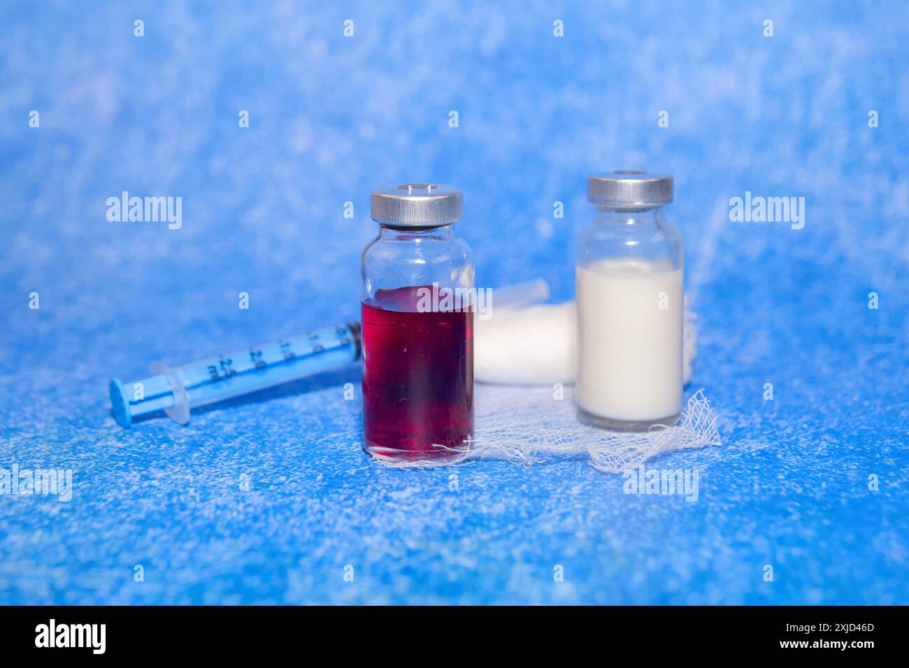 Zwei Impfstofffläschchen, eine rote, eine klare, ruhen auf einem Mulltupfer mit einer Spritze in der Nähe. Bereit zur Immunisierung Stockfoto Zwei Impfstofffläschchen, eine rote, eine klare, ruhen auf einem Mulltupfer mit einer Spritze in der Nähe. Bereit zur Immunisierung Stockfoto