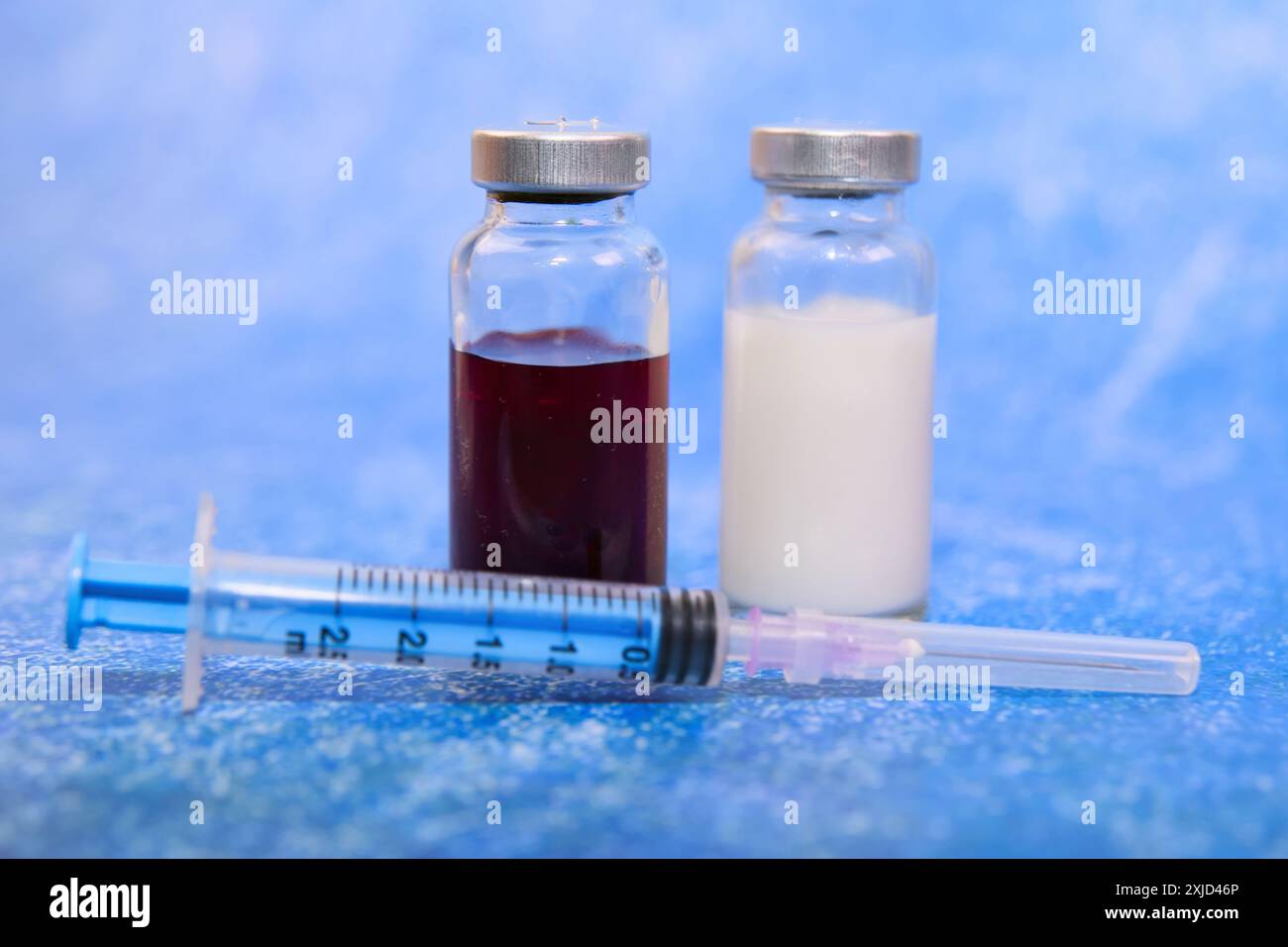 Zwei Impfstofffläschchen, eine rote, eine klare, ruhen auf einem Mulltupfer mit einer Spritze in der Nähe. Bereit zur Immunisierung. Stockfoto Zwei Impfstofffläschchen, eine rote, eine klare, ruhen auf einem Mulltupfer mit einer Spritze in der Nähe. Bereit zur Immunisierung. Stockfoto