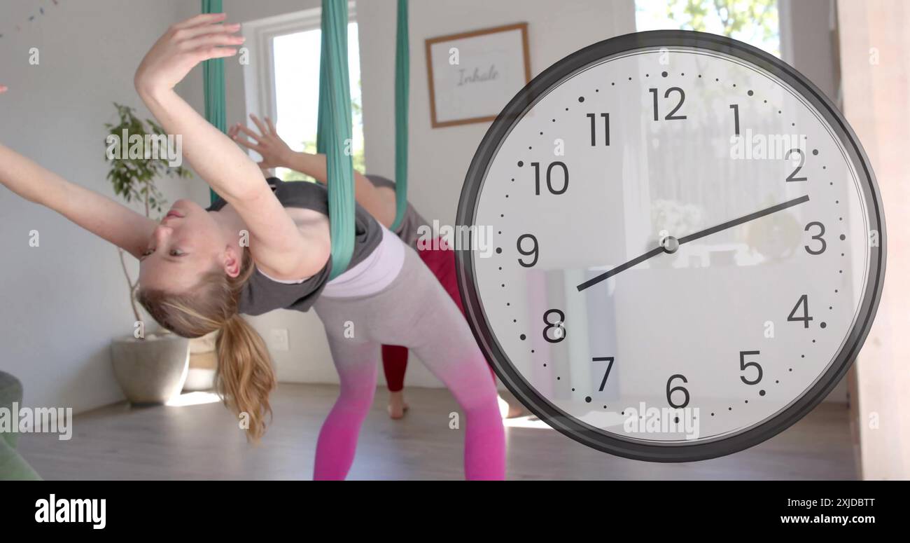 Bild einer schnell beweglichen Uhr über kaukasische Lehrerin und Teenager-Mädchen, die Luft-Yoga machen Stockfoto