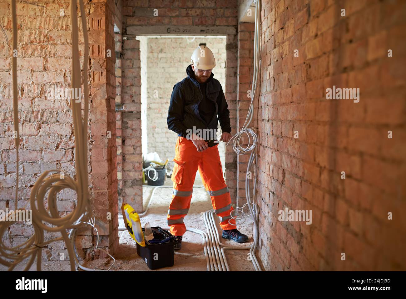 Elektriker, der Drahtschleifer bei der Installation von elektrischen Leitungen verwendet, in Gebäuden, die gerade renoviert werden, mit freiliegenden Ziegelwänden und unbehandelter Oberfläche Stockfoto