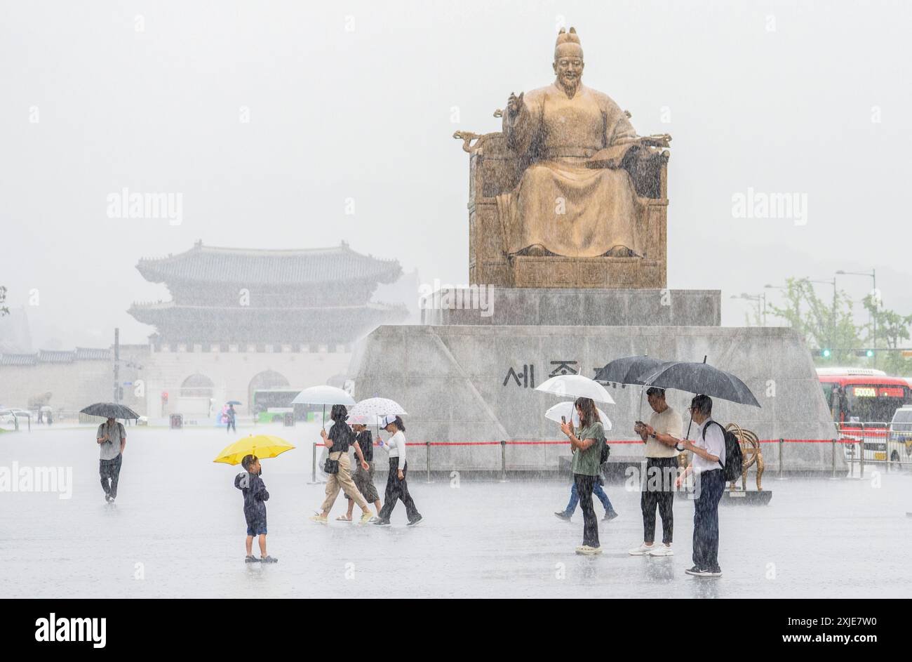 Seoul, Südkorea. Juli 2024. Menschen, die Regenschirme halten, um sich vor Regen zu schützen, spazieren durch eine Statue von Sejong dem Großen am zentralen Gwanghwamun-Platz in Seoul. Sintflutartige Regengüsse überschwemmten das größere Gebiet von Seoul und angrenzende Regionen am 18. Juli, was zur Evakuierung der Bewohner aufgrund von geschwollenen Bächen und der Schließung von Autobahnen, einer Brücke in Seoul und nahegelegenen U-Bahn-Diensten führte. Quelle: SOPA Images Limited/Alamy Live News Stockfoto