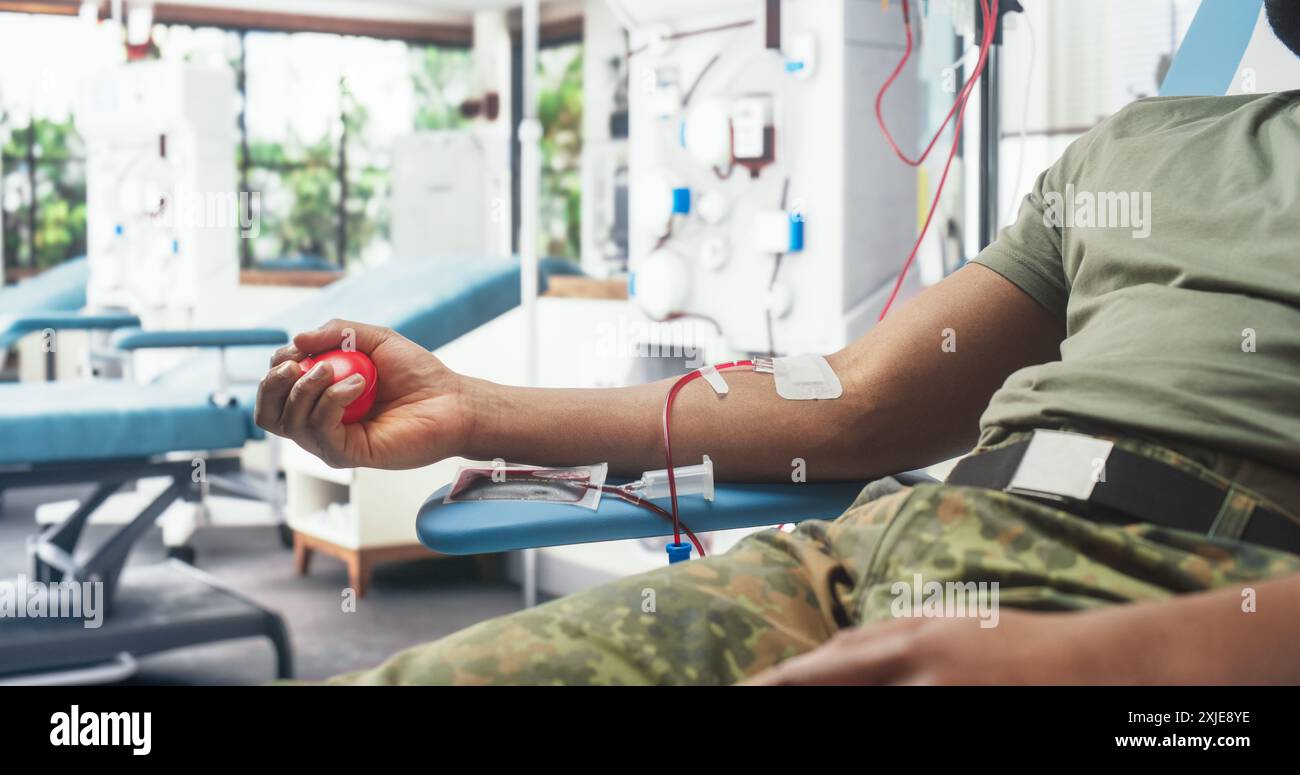 Nahaufnahme Der Hand Des Schwarzen Soldaten Mit Angebrachtem Katheter Im Militärkrankenhaus. Mutige Afrikanische Männliche Truppe, Die Den Roten Ball Durchquert, Um Blut Durch Den Schlauch In Den Beutel Zu Pumpen. Mann Spendet An Verwundete Kameraden. Stockfoto