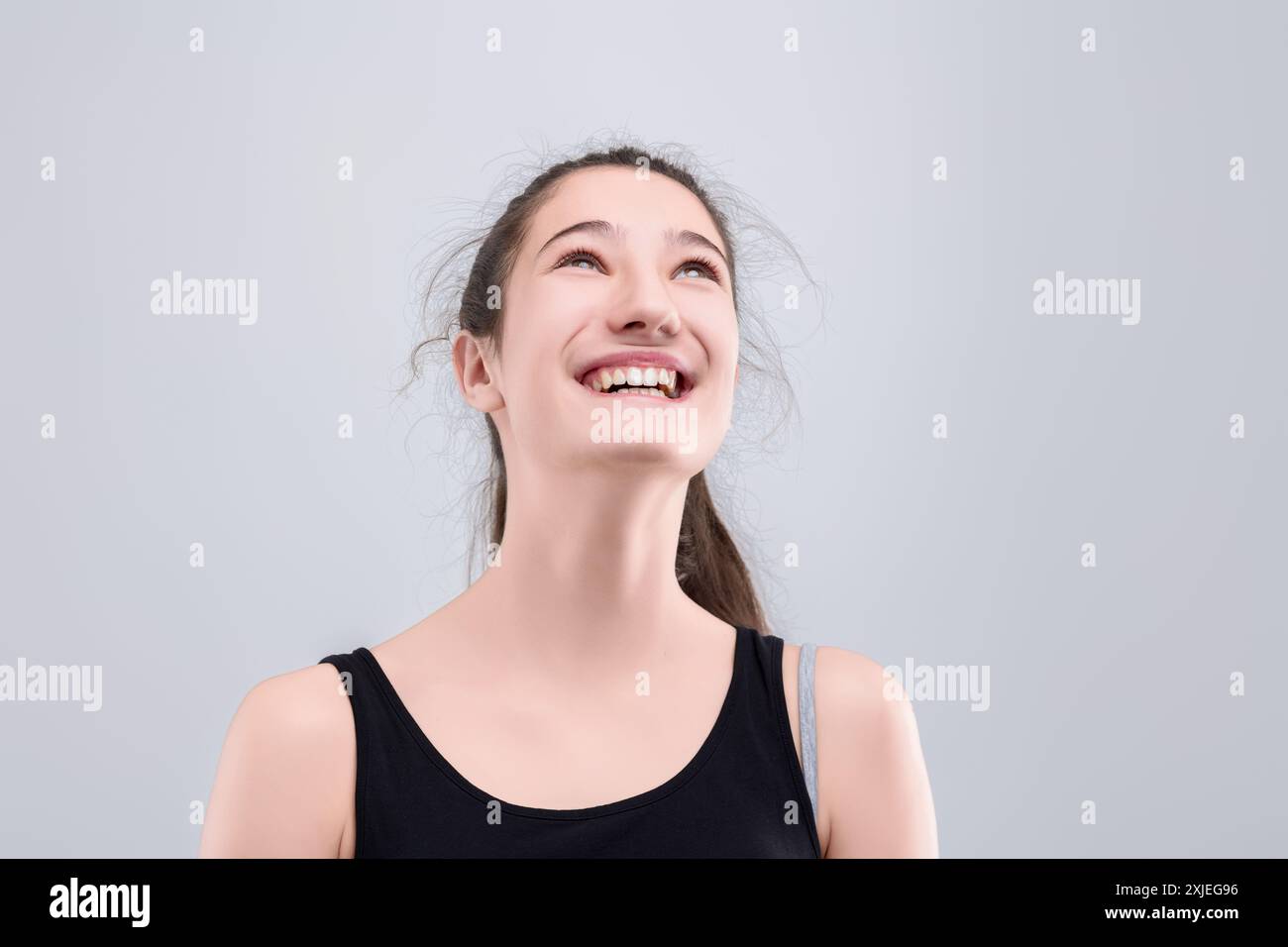 Die junge Frau lächelt glücklich und blickt mit Freude und Optimismus vor grauem Hintergrund auf. Sie strahlt Selbstvertrauen und Hoffnung aus, perfekt für die Vermittlung von Glück Stockfoto