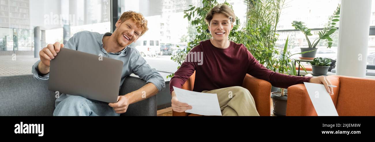 Zwei männliche Studenten sitzen auf einer Couch, fokussiert auf einem Laptop-Bildschirm. Stockfoto