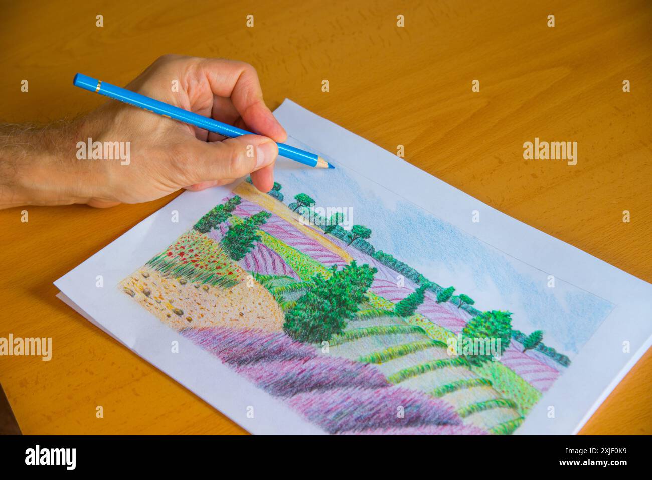 Die Hand des Mannes zeichnet eine Landschaft mit Farbstiften. Stockfoto