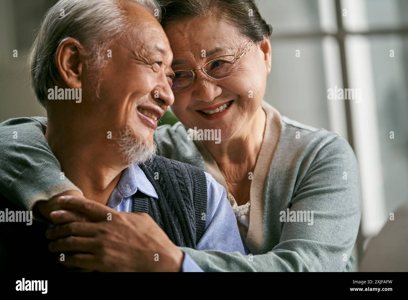 Porträt eines glücklichen liebenden asiatischen Seniorenpaares, das zu Hause auf der Couch sitzt Stockfoto