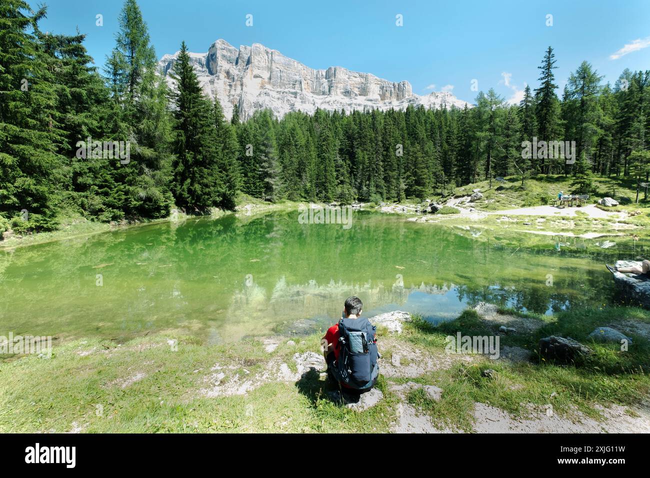 Der Wanderer macht eine Pause am Ufer eines unberührten Bergsees mit einem majestätischen Bergmassiv im Hintergrund, dem See Carezza, Italien Stockfoto