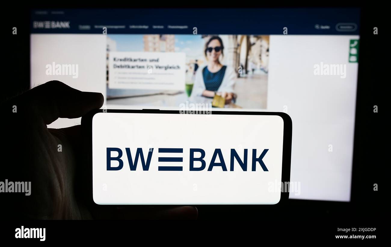 Person mit Mobiltelefon mit Logo der deutschen Firma Baden-Wuerttembergische Bank (BW-Bank) vor der Business-Webseite. Schwerpunkt auf dem Display des Telefons. Stockfoto