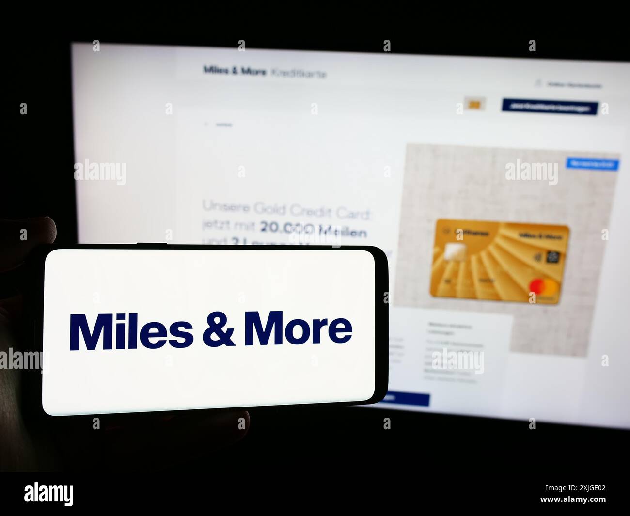 Person mit Mobiltelefon mit Logo des Vielfliegerprogramms Meilen und mehr (Lufthansa) vor der Business-Webseite. Schwerpunkt auf dem Display des Telefons. Stockfoto