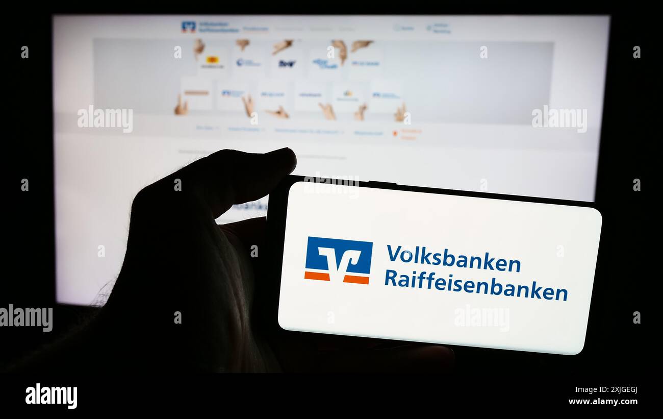 Person mit Smartphone mit Logo des deutschen Banknetzes Volksbanken Raiffeisenbanken vor der Website. Schwerpunkt auf dem Display des Telefons. Stockfoto