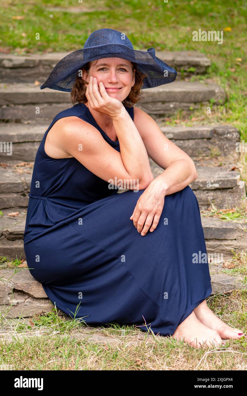 Eine 50-55-jährige Frau in blauem Kleid sitzt auf Steintreppen Stockfoto