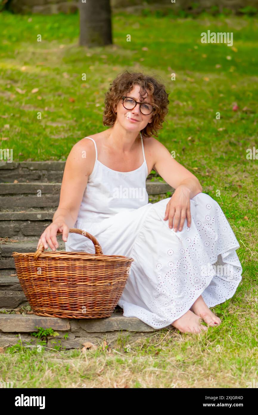 Frau in weißem Kleid sitzt auf Steinstufen mit Korb aus Weide Stockfoto
