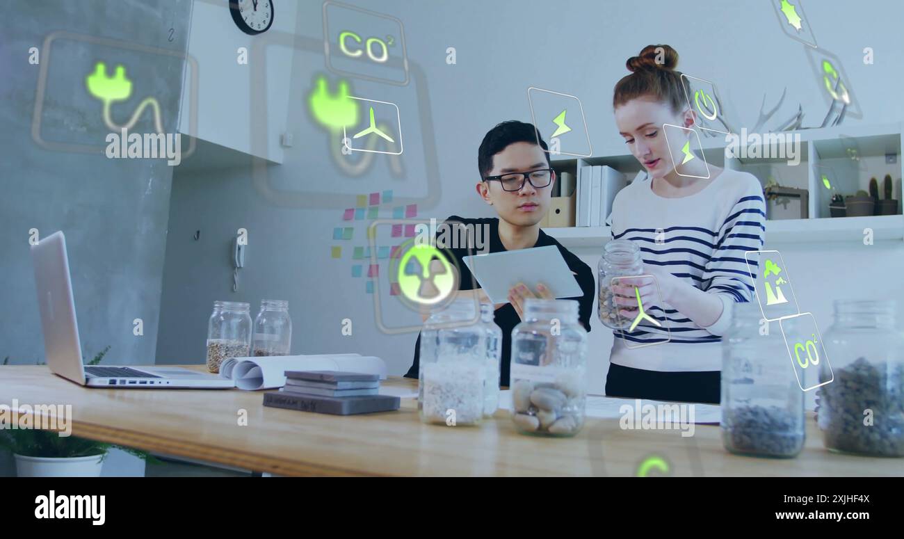 Bild von ökologischen Symbolen über verschiedenen Kollegen, die ein Tablet im Büro verwenden Stockfoto