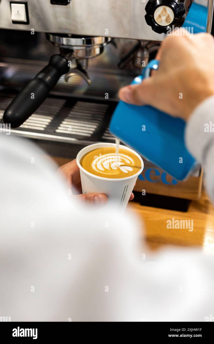 Milch wird während des Zubereitungsprozesses in einen Kaffee gegossen. Stockfoto