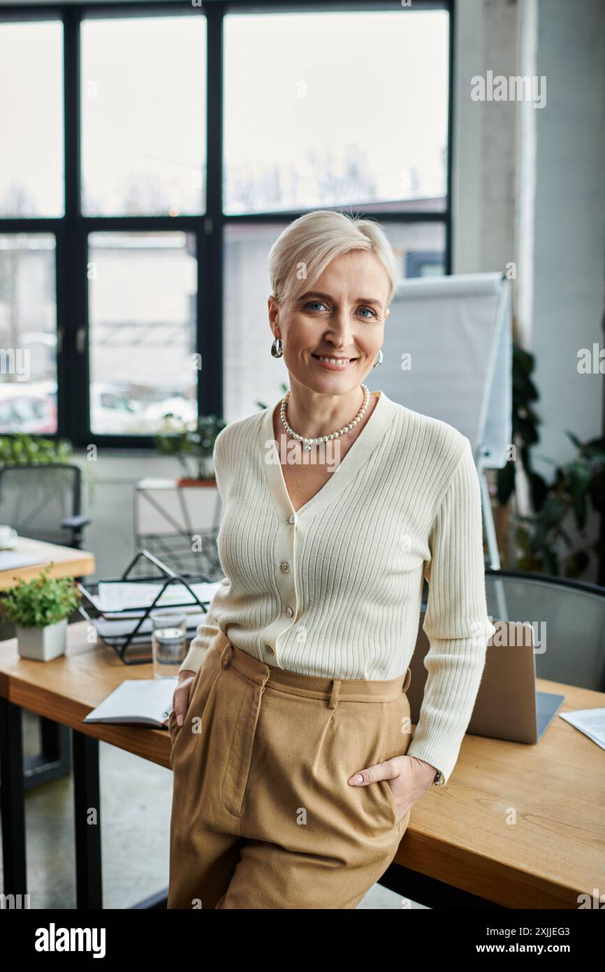 Eine Geschäftsfrau mittleren Alters mit kurzen Haaren steht selbstbewusst in einem modernen Büro vor einem eleganten Schreibtisch. Stockfoto