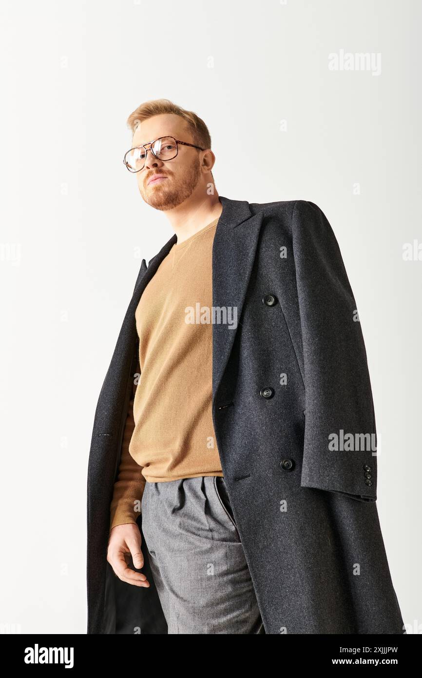 Hübscher Mann in stilvollem langem Mantel und Brille, der selbstbewusst posiert. Stockfoto