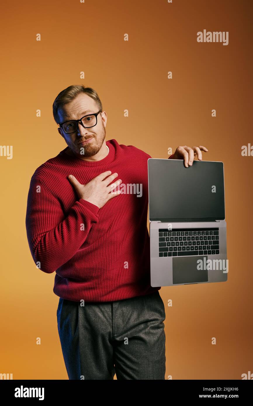 Ein stilvoller Mann in einem roten Pullover hält selbstbewusst ein Notebook. Stockfoto