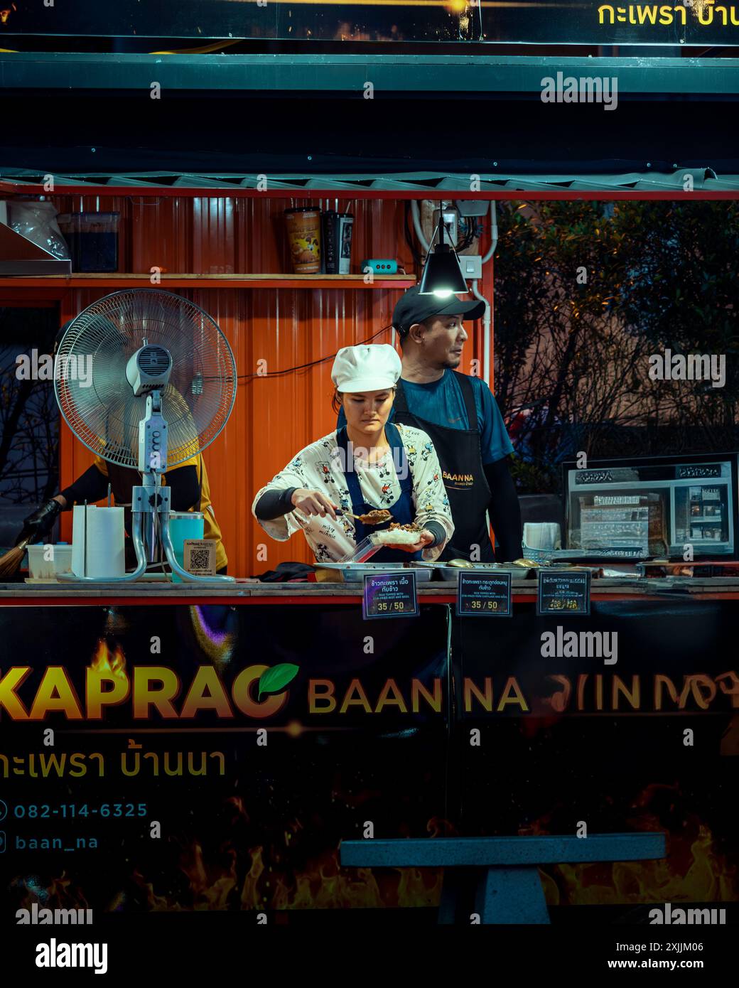 Viel beschäftigtes Thai-Mädchen, das ein traditionelles thailändisches Gericht am Straßenstand zubereitet Stockfoto