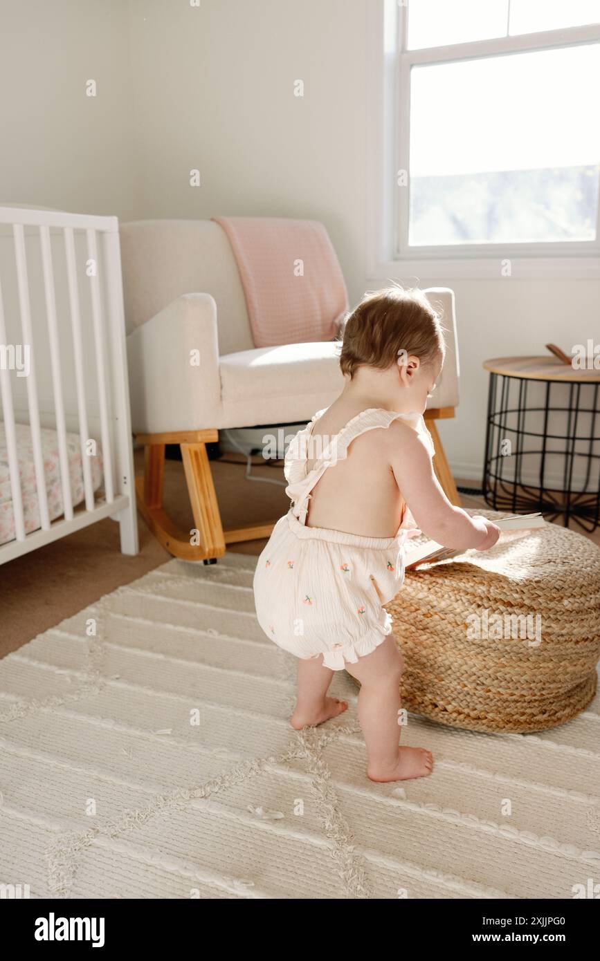 Ein Kind erkundet das sonnige Kinderzimmer, während es mit einem Buch spielt Stockfoto