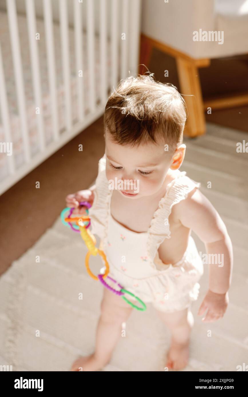 Neugieriges Kleinkind, das im Kinderzimmer mit farbenfrohen Spielzeugen experimentiert und spielt Stockfoto