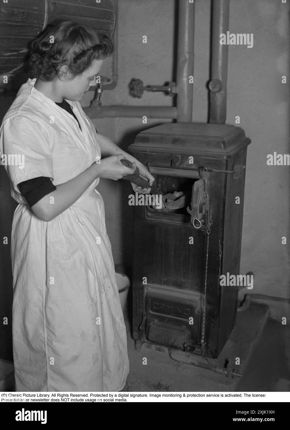 Leben in den 1940ern Eine junge Frau, die als Dienstmädchen arbeitete, und der Fotograf folgten ihr während eines Arbeitstages, beginnend mit ihr im Keller des Hauses, wo sie ein Feuer im Kessel machte. Schweden 1940. Kristoffersson Ref. 55-6 Stockfoto