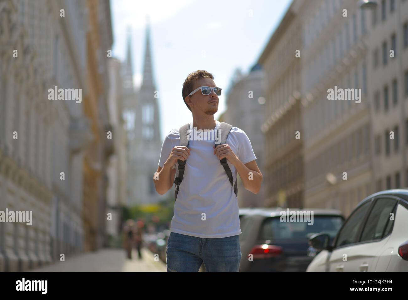 Ein Mann mit weißer Sonnenbrille und grauem Rucksack auf der Straße in Wien an einem heißen, sonnigen Sommertag. Tourismus- und Sightseeing-Konzept. Stockfoto