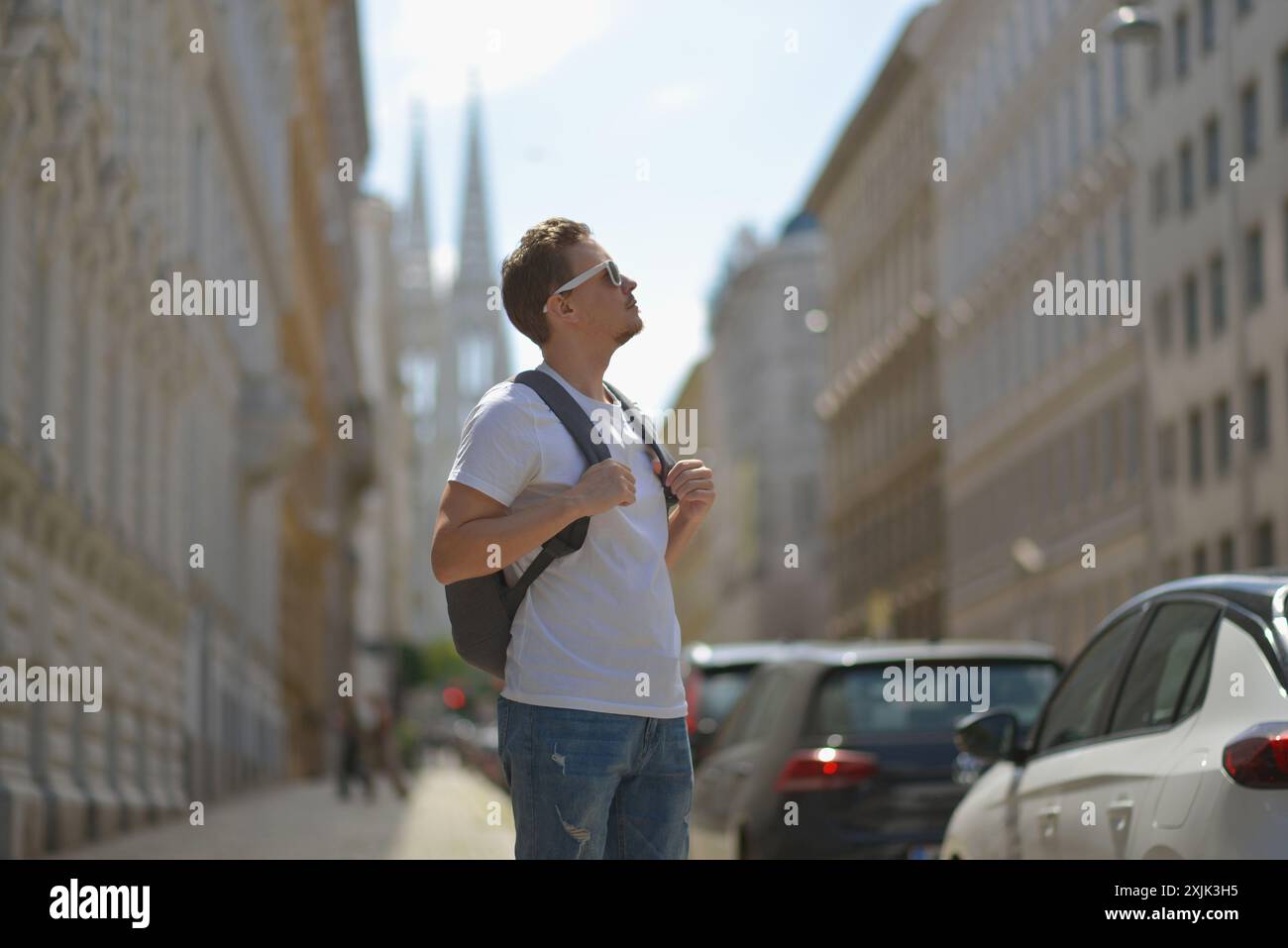 Ein Mann mit weißer Sonnenbrille und grauem Rucksack auf der Straße in Wien an einem heißen, sonnigen Sommertag. Tourismus- und Sightseeing-Konzept. Stockfoto