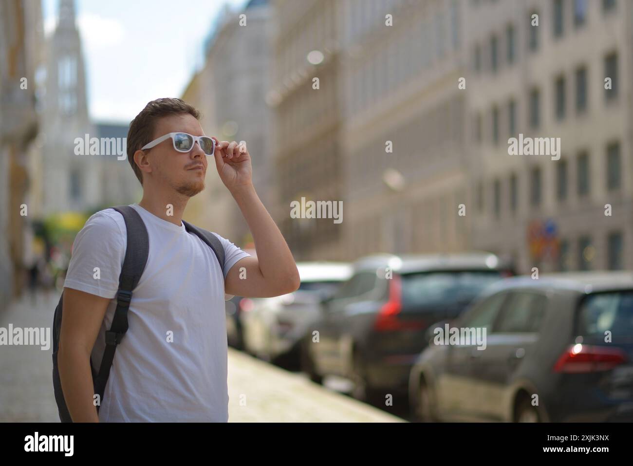 Ein Mann mit weißer Sonnenbrille und grauem Rucksack auf der Straße in Wien an einem heißen, sonnigen Sommertag. Tourismus- und Sightseeing-Konzept. Stockfoto