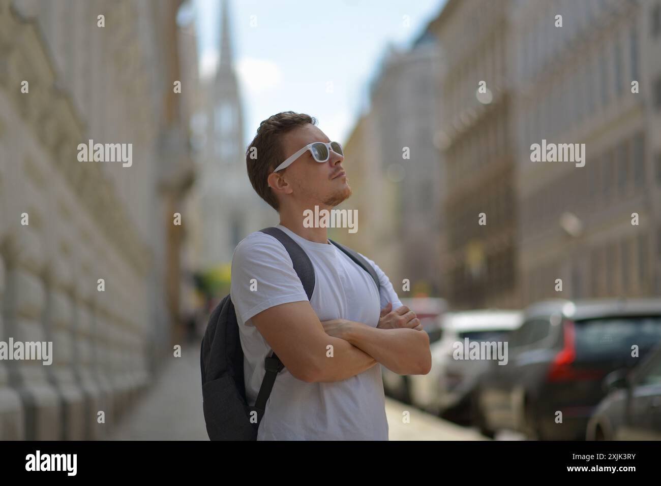 Ein Mann mit weißer Sonnenbrille und grauem Rucksack auf der Straße in Wien an einem heißen, sonnigen Sommertag. Tourismus- und Sightseeing-Konzept. Stockfoto