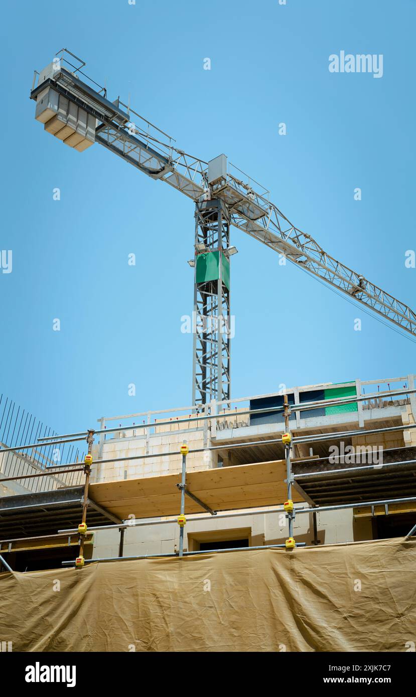 Ein Turmkran befindet sich neben einem im Bau befindlichen mehrstöckigen Gebäude, das an klaren Tagen den industriellen Fortschritt und die Entwicklung zeigt. Stockfoto