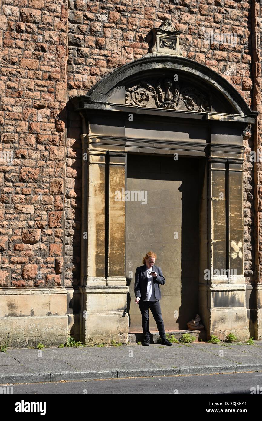 Frau, die eine Pause macht, steht mit Telefon und Rauch in der Tür des alten großen Gebäudes, Großbritannien Stockfoto