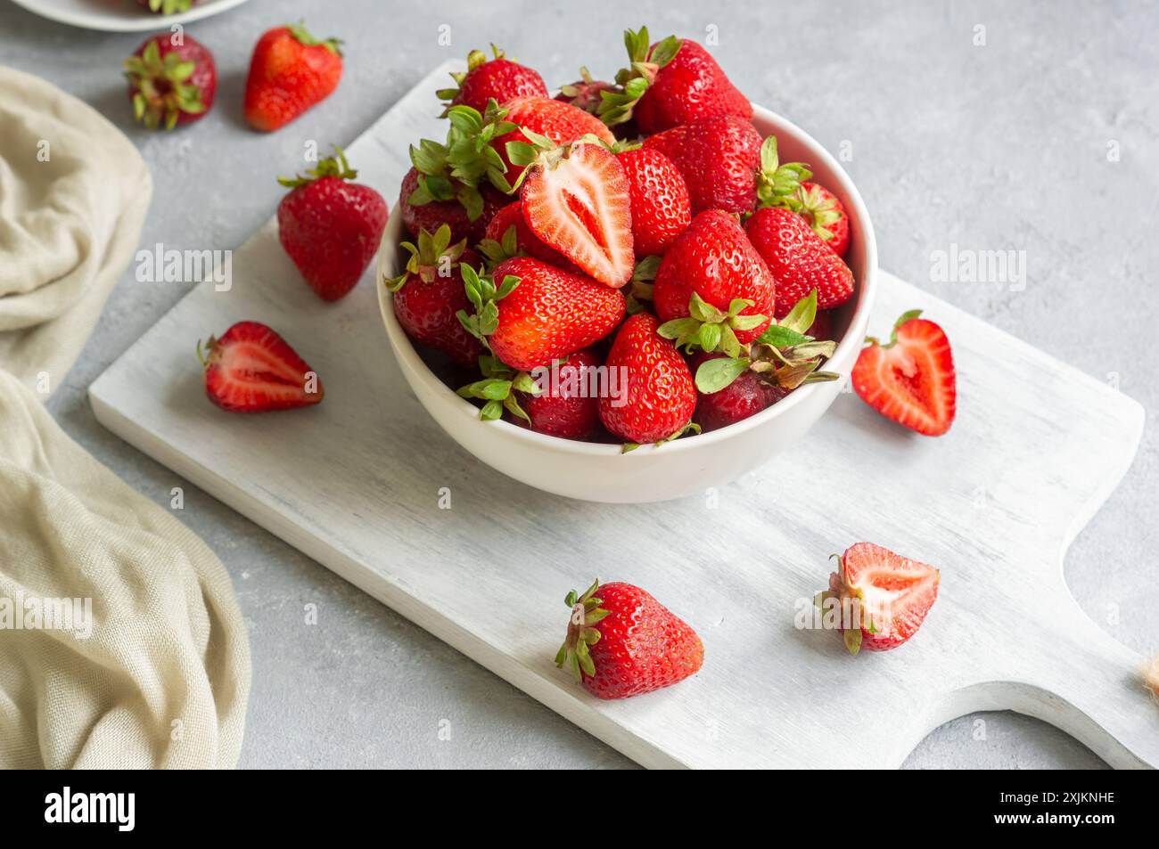 Frische reife Erdbeeren in weißer Schüssel auf weißem Schneidebrett auf rustikalem Tisch, rote Sommerfrüchte Stockfoto