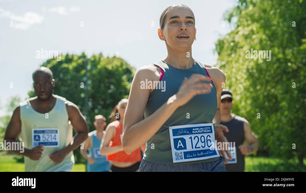 Porträt einer Frau, die in einem Park läuft und an einem Marathon teilnimmt. Starke sportliche Joggingerin, die andere Läufer mit Entschlossenheit für den ersten Platz in der Ziellinie fährt Stockfoto