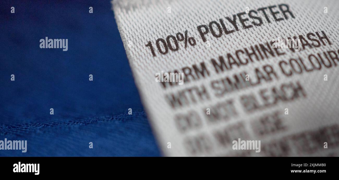 Bekleidungsetikett aus Polyester mit Hinweisen zur Wäschepflege auf blauem Hemdtrikot Stockfoto