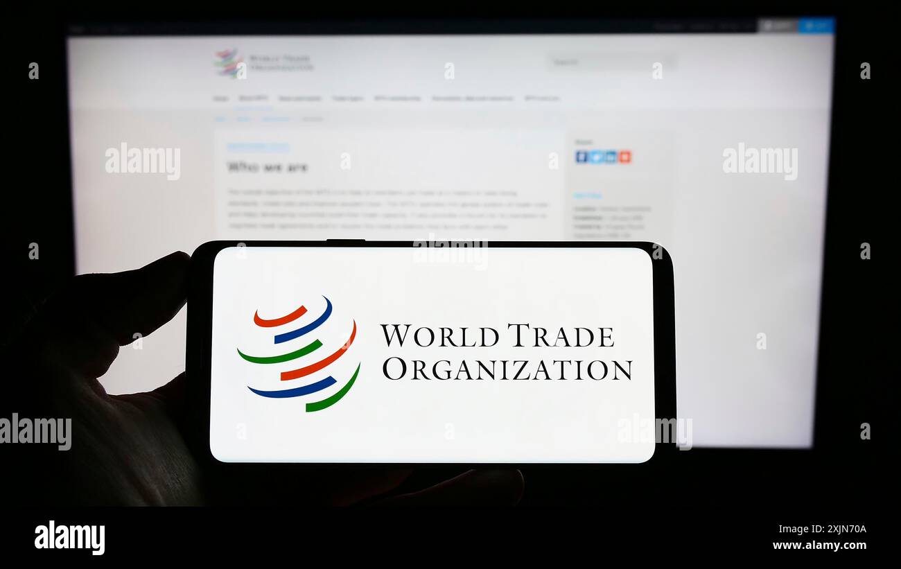 Stuttgart, Deutschland, 25.03.2023: Person, die ein Mobiltelefon mit dem Logo der Welthandelsorganisation (WTO) auf dem Bildschirm vor der Webseite hält. Konzentrieren Sie sich auf das Telefon Stockfoto Stuttgart, Deutschland, 25.03.2023: Person, die ein Mobiltelefon mit dem Logo der Welthandelsorganisation (WTO) auf dem Bildschirm vor der Webseite hält. Konzentrieren Sie sich auf das Telefon Stockfoto