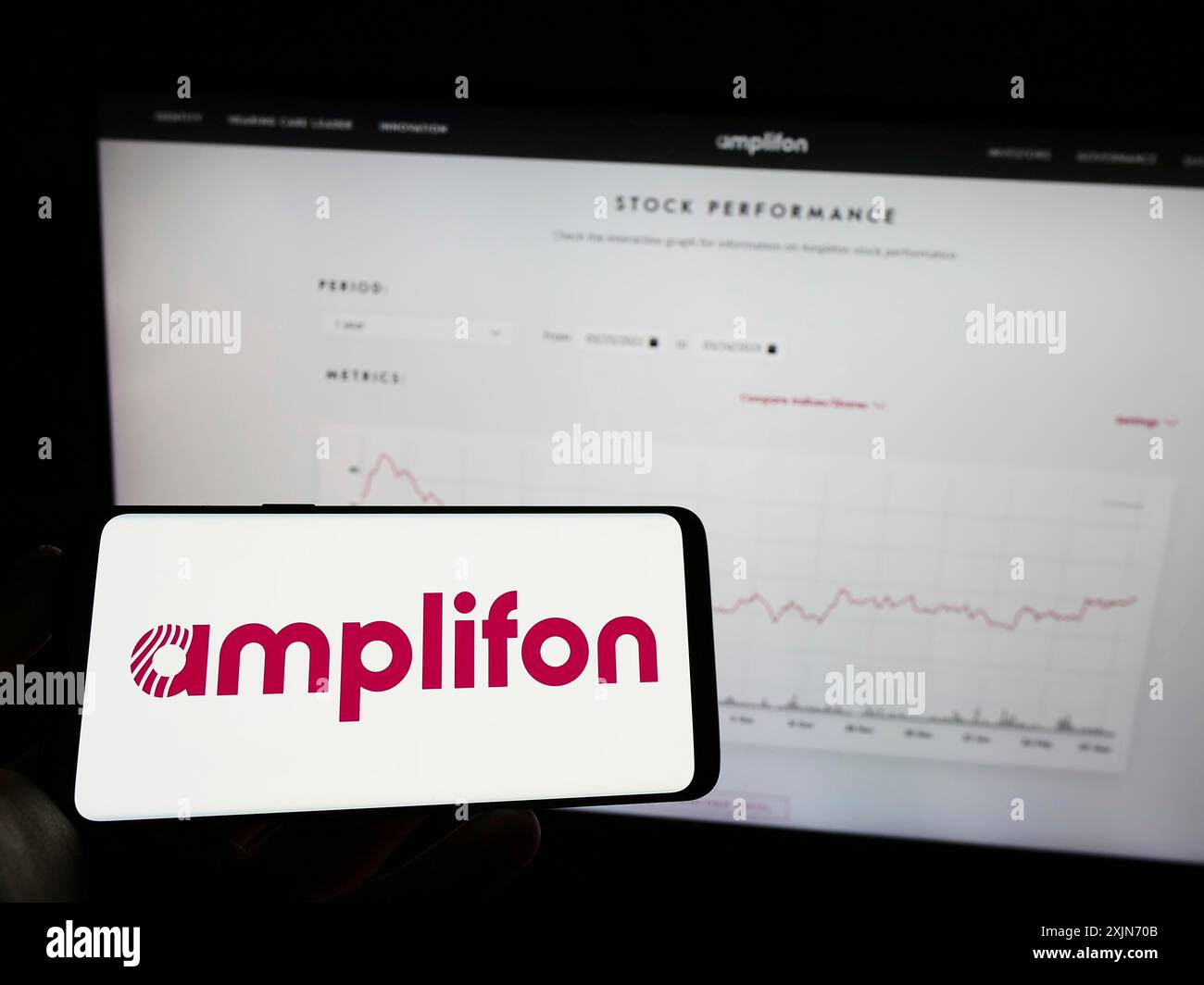 Stuttgart, 25.03.2023: Person, die ein Mobiltelefon mit dem Logo des italienischen Hörgeräteunternehmens Amplifon S.p.A. auf dem Bildschirm vor der Webseite hält. Stockfoto