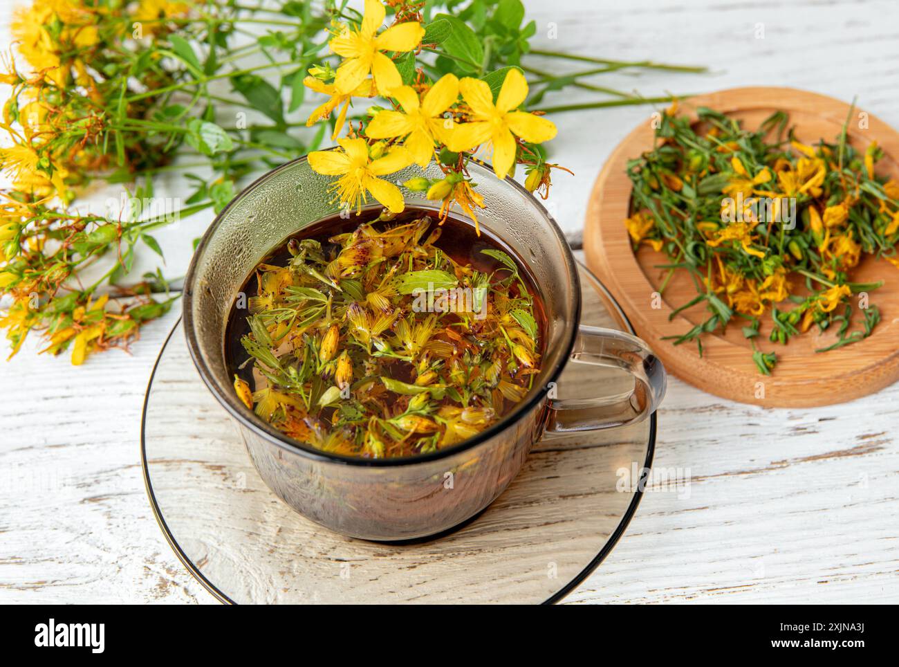 Hypericum perforatum, auch bekannt als Johanniskraut, Johanniskraut oder Johanniskraut Kräutertee in Glas auf weißem Holzbrett. Stockfoto